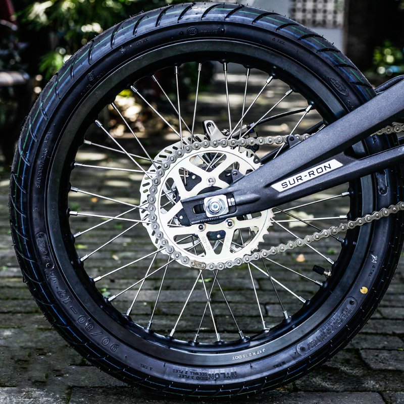Close-up of a motorcycle wheel with chain and 'Sur-Ron' brand name.